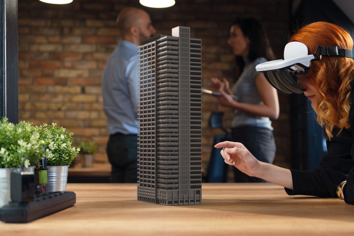 A person interacts with a model of a building using virtual reality glasses.