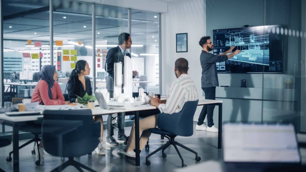 Alt Text: A diverse group of workers reviewing digital design plans in a modern architecture and design firm office.